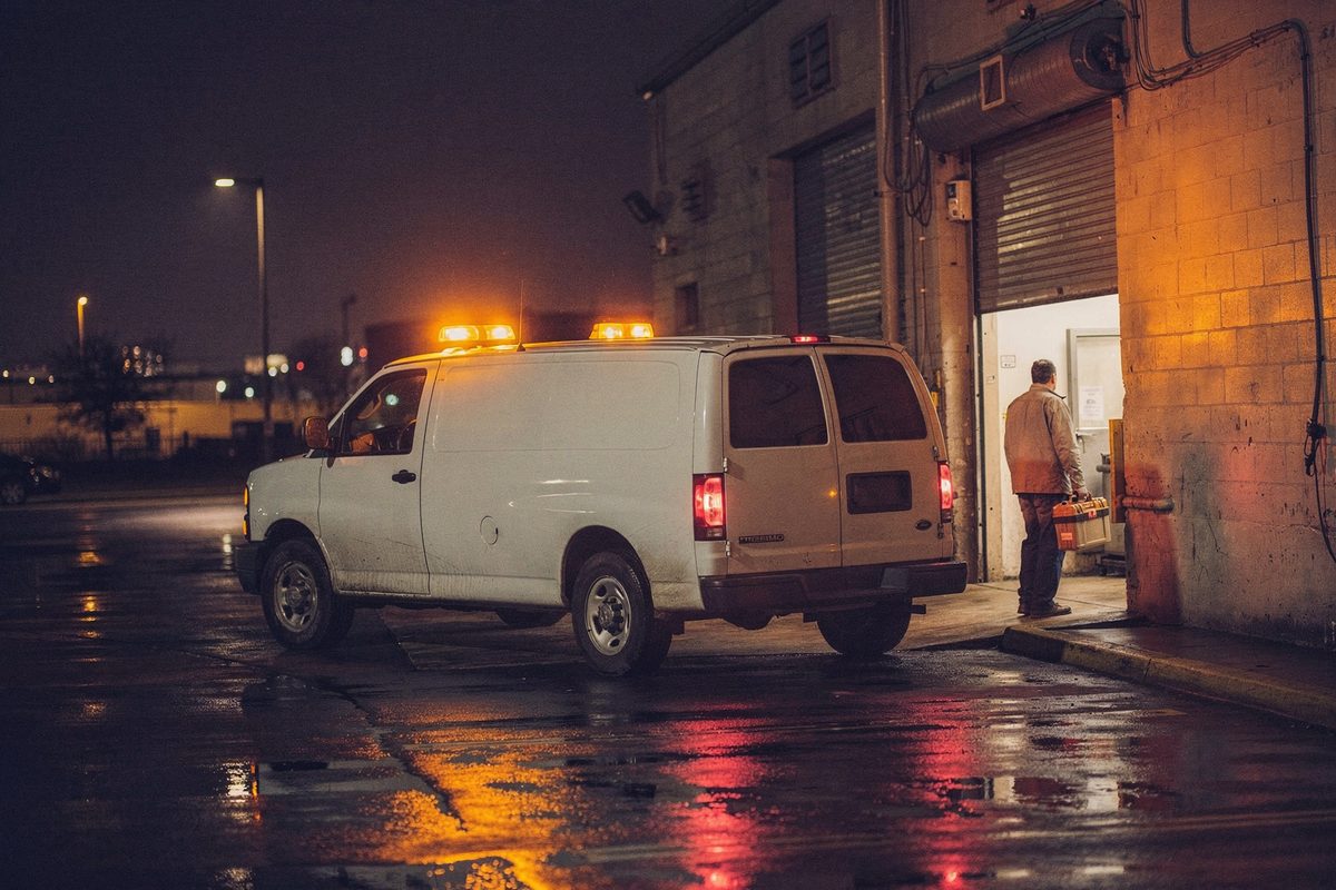Service van parked at a lit doorway during a night emergency repair callout